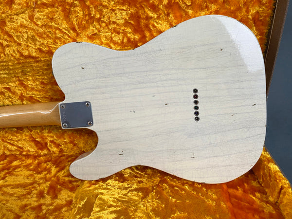 Vintage white electric guitar body with aged finish and string ferrules, displayed in a plush orange guitar case interior.