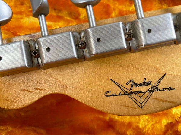 Close-up of vintage Fender Custom Shop guitar headstock tuners with worn metal tuning machines and natural maple wood background on orange plush fabric
