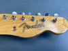 Close-up of Fender Telecaster guitar headstock with tuning pegs and strings on gray background