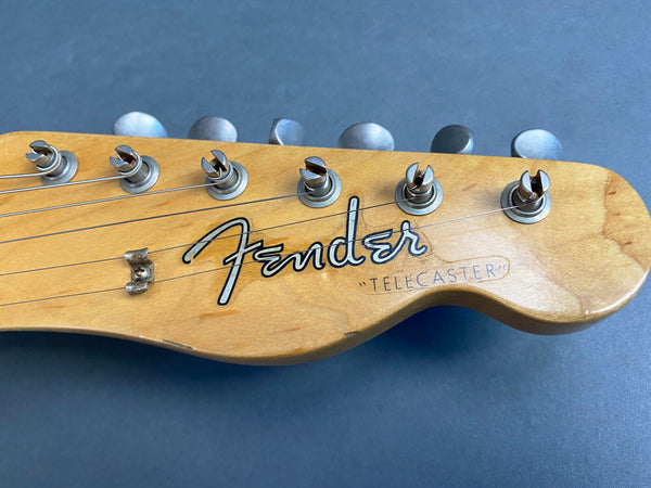 Close-up of Fender Telecaster guitar headstock with tuning pegs and strings on gray background