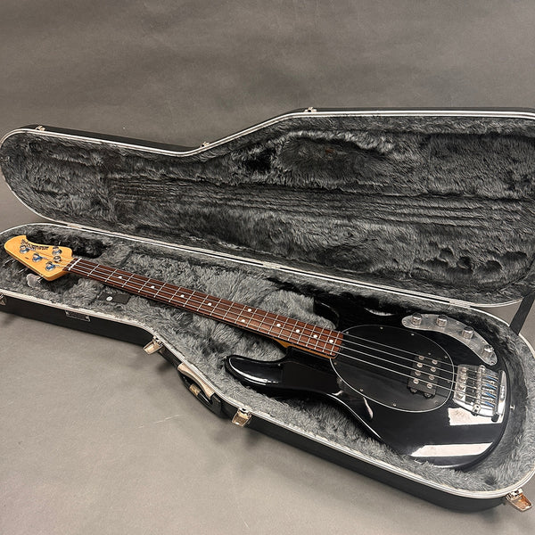 Black electric bass guitar with rosewood fretboard in open hard shell case with gray plush interior liner