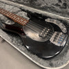 Black electric bass guitar with rosewood fretboard, chrome bridge and control knobs, resting in a gray plush-lined hard case