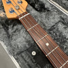 Close-up of bass guitar neck and headstock showing rosewood fretboard and tuning pegs inside a plush gray guitar case