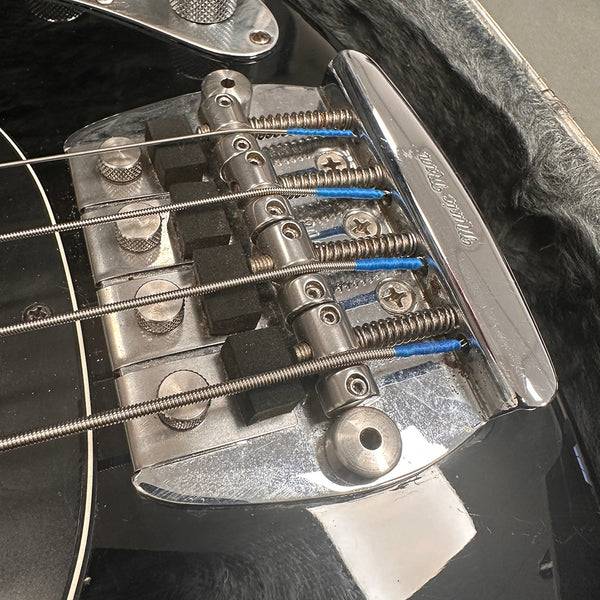 Close-up of metal bridge and strings on black electric bass guitar with chrome hardware and blue string windings