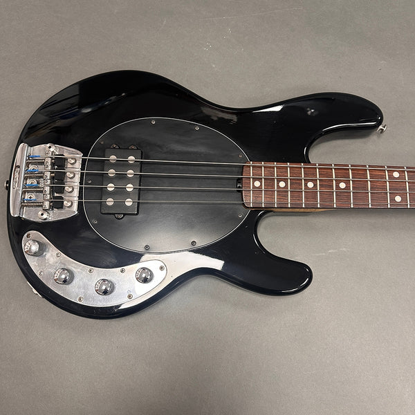 Black electric bass guitar with rosewood fretboard, four strings, and chrome control knobs on a gray background