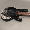 Black electric bass guitar with rosewood fingerboard and chrome control knobs on gray background