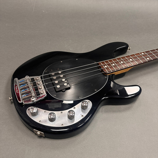 Black electric bass guitar with chrome control knobs and brown fretboard on gray background