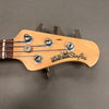 Close-up of Ernie Ball Music Man StingRay bass guitar headstock with tuning pegs and strings against gray background