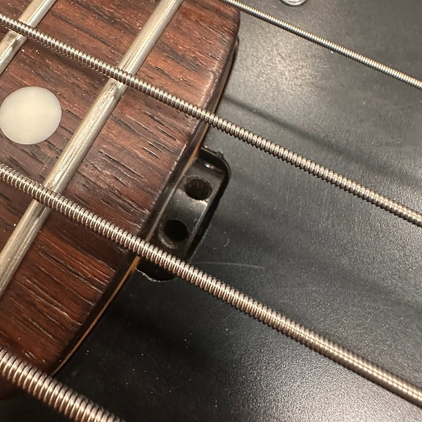 Close-up of bass guitar strings and dark wood fretboard with metal frets and white dot inlay on Coffee House Guitars instrument