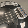 Close-up of black electric bass guitar bridge, pickup, and control knobs showing metal strings and hardware details