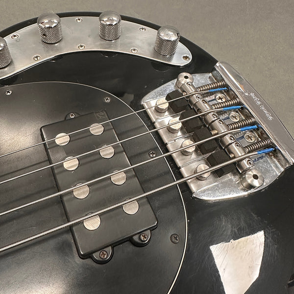 Close-up of black electric bass guitar bridge, pickup, and control knobs showing metal strings and hardware details