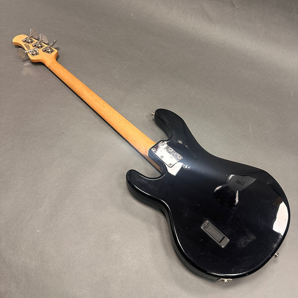 Black electric bass guitar with maple neck and chrome tuning pegs, rear view on gray background