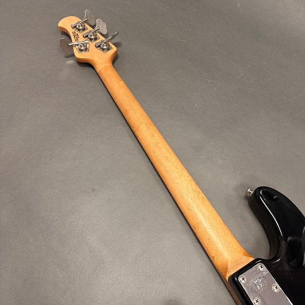 Maple neck and headstock of black electric bass guitar with chrome tuning pegs and metal neck plate against gray background