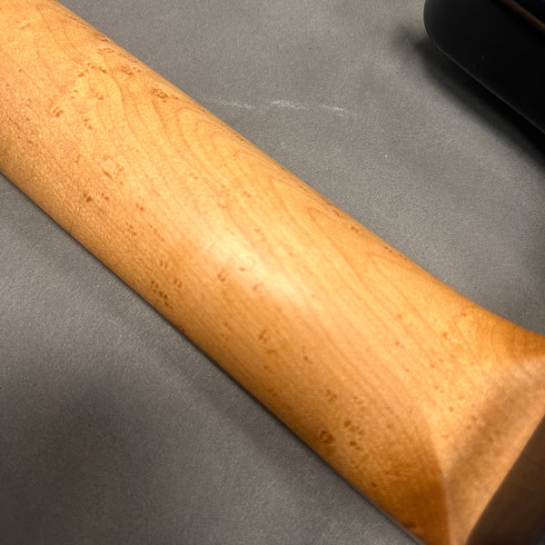 Close-up of a light-colored maple guitar neck with visible wood grain and birdseye figure on a gray background