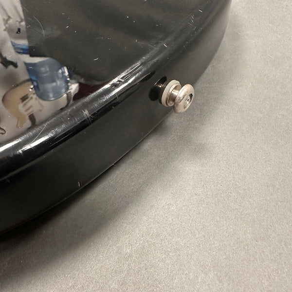 Close-up of black guitar body with strap button and scratches on the finish