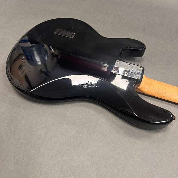 Back view of black electric guitar body with natural wood neck and chrome neck plate on gray surface