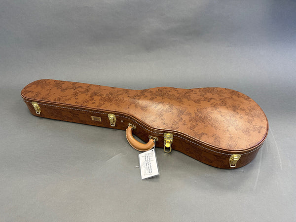 Brown vintage-style hard guitar case with leather handle and gold latches on gray background