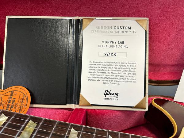 Gibson Custom Certificate of Authenticity for Murphy Lab Ultra Light Aging guitar with serial number 81123 inside red guitar case with partially visible guitar neck and vintage guitar strings packaging