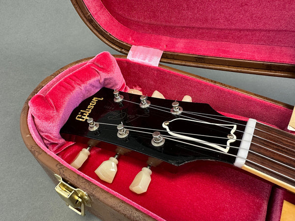 Close-up of Gibson guitar headstock with tuning pegs inside vintage red velvet-lined guitar case