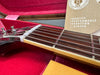 Close-up of Gibson guitar neck and strings inside red velvet-lined guitar case with Gibson Historic Collection warranty card visible