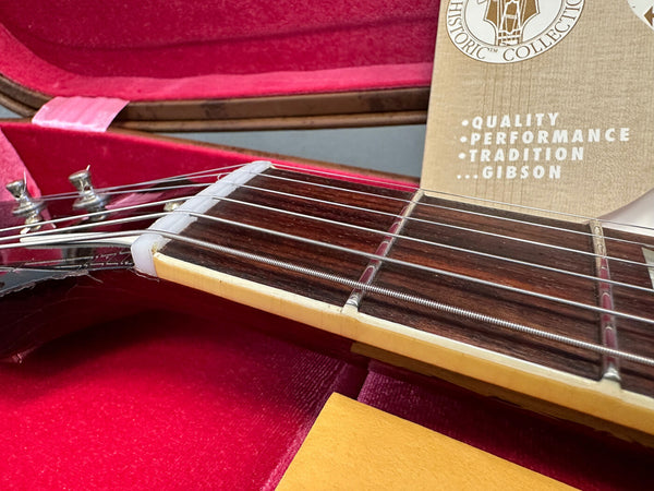 Close-up of Gibson guitar neck and strings inside red velvet-lined guitar case with Gibson Historic Collection warranty card visible