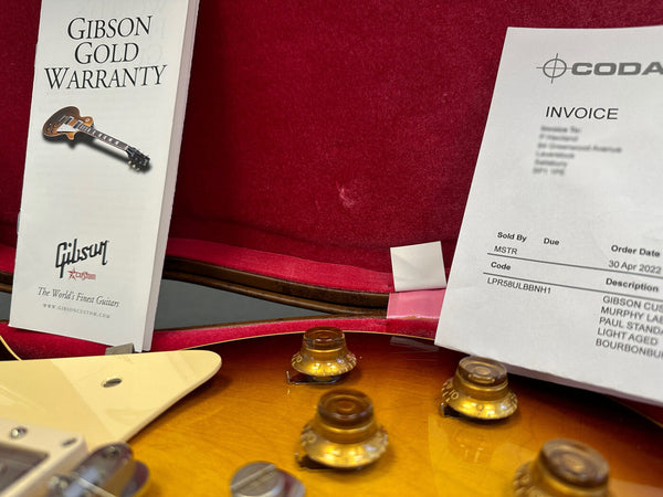 Close-up of Gibson guitar control knobs with Gibson Gold Warranty booklet and Coda invoice in red velvet guitar case interior