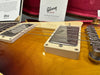 Close-up of sunburst Gibson Les Paul electric guitar pickups and strings with Gibson Custom certificate and red velvet case interior in background