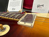 Close-up of Gibson Custom Shop electric guitar with aged finish and metal pickup, toggle switch, and vintage Gibson Custom papers in the background