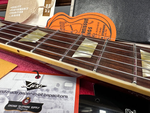 Close-up of Gibson guitar rosewood fretboard with mother of pearl block inlays, guitar strings, and accompanying Gibson reissue strings and Luxe handmade paper-in-oil capacitors tags