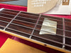 Close-up of Gibson guitar rosewood fretboard with mother-of-pearl inlay, metal frets, and steel strings on red velvet background