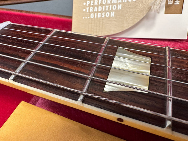 Close-up of Gibson guitar rosewood fretboard with mother-of-pearl inlay, metal frets, and steel strings on red velvet background
