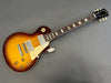 Gibson Les Paul electric guitar with sunburst finish, dual humbucker pickups, rosewood fretboard, and cream pickguard on gray background