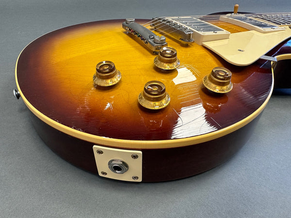 Close-up of sunburst electric guitar body with four amber control knobs and bridge on gray background