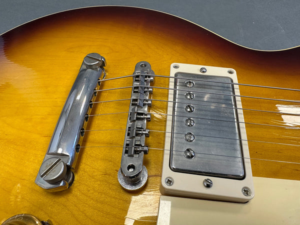 Close-up of sunburst electric guitar bridge, chrome Tune-O-Matic bridge and tailpiece with humbucker pickup and metal strings on a glossy wooden body