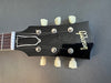 Close-up of black Gibson Les Paul guitar headstock with vintage-style tuning pegs and white logo on dark background