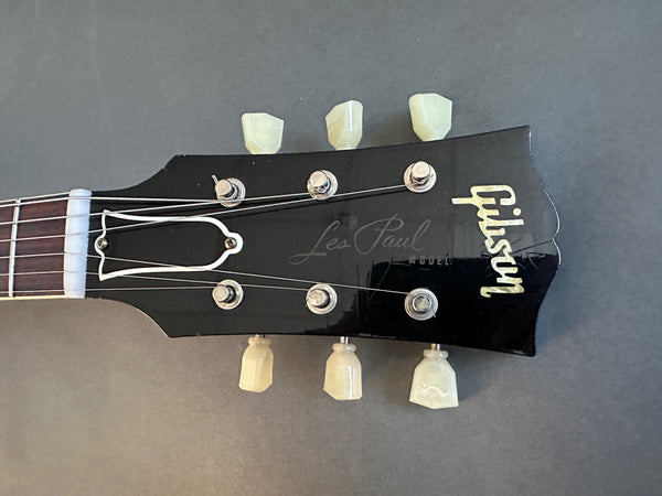 Close-up of black Gibson Les Paul guitar headstock with vintage-style tuning pegs and white logo on dark background