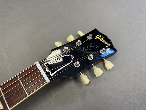 Close-up of Gibson Les Paul guitar headstock with tuning pegs, truss rod cover, and logo on black finish against gray background