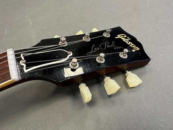 Close up of Gibson Les Paul electric guitar black headstock with tuners and strings on gray background