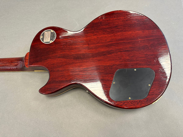 Back of Gibson electric guitar with dark red wood finish and black control cavity cover against gray background