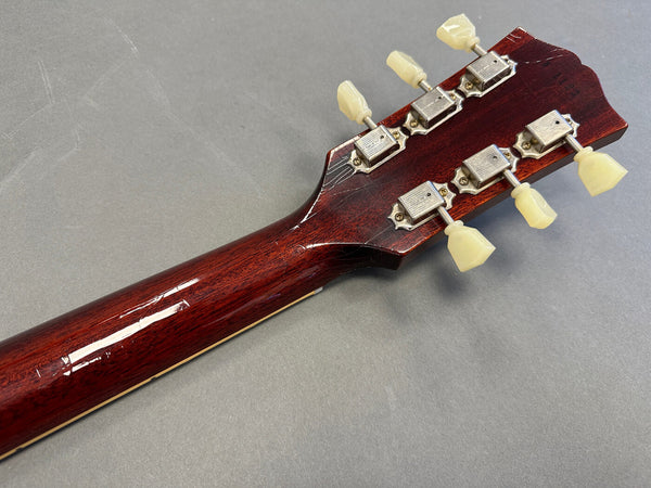 Back of vintage wooden guitar headstock with six cream tuning pegs on gray background, showing neck and tuning machines