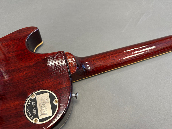 Close-up of the back and neck joint of a Gibson Custom electric guitar with dark red wood finish and Gibson Custom metal backplate, showing wood grain and neck contour.