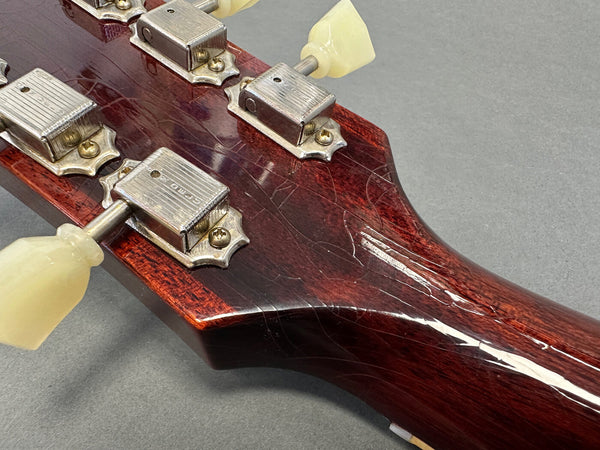 Close-up of vintage dark wood guitar headstock with aged white tuning pegs and metal tuning machines on gray background