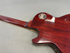 Back of Gibson Les Paul electric guitar with worn cherry red finish and metal control cavity cover, showing wood grain and neck joint details