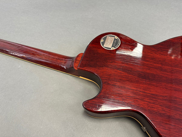 Back of Gibson Les Paul electric guitar with worn cherry red finish and metal control cavity cover, showing wood grain and neck joint details