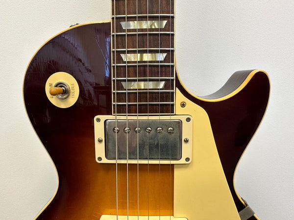 Close-up of sunburst electric guitar body with cream-colored pickup ring and toggle switch labeled rhythm and treble against a white background