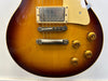 Close-up of sunburst electric guitar body showing metal bridge, humbucker pickup, cream pickguard, and four amber control knobs