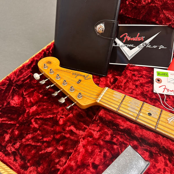Fender Stratocaster guitar headstock with vintage tuning pegs in plush red lined guitar case with Fender custom shop card and black leather accessory pouch.
