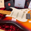 Close-up of vintage sunburst Fender Stratocaster electric guitar showing maple neck, white pickguard, three single-coil pickups, tone and volume knobs, and worn finish on red plush guitar case lining with Fender certification and accessory box in background.
