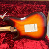Back of sunburst Fender Stratocaster electric guitar with cream tremolo cavity cover on red plush Fender guitar case interior