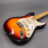 Vintage sunburst electric guitar with maple fretboard, white pickguard, and three single-coil pickups on gray background